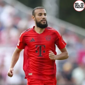 Manchester United's Noussair Mazraoui, wearing a Bayern Munich jersey, standing confidently on the pitch after his transfer from Bayern Munich to Man Utd